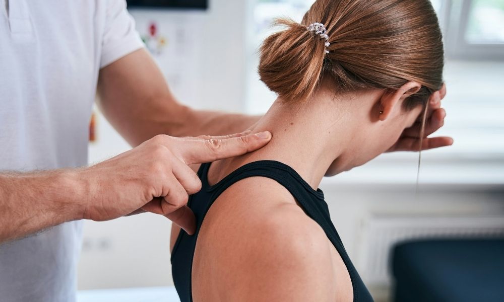 A physical therapist palpates the neck of a patient who is leaning forward.