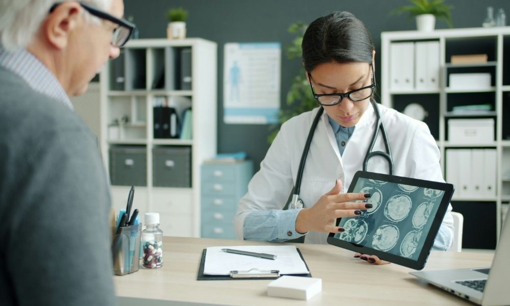 ASA (19) A doctor showing a patient a medical brain scan on a tablet in an office.