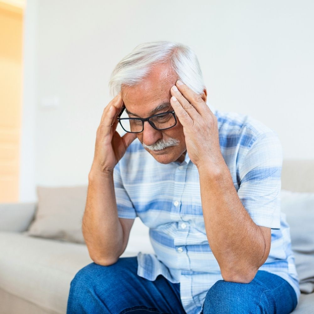 ASA (20) An older man with glasses sits on a sofa with his head in his hands, looking distressed.