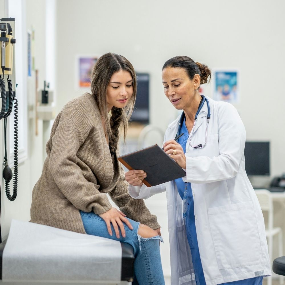 ASA (22) A female doctor in a white coat shows a tablet to a patient sitting on an exam table.