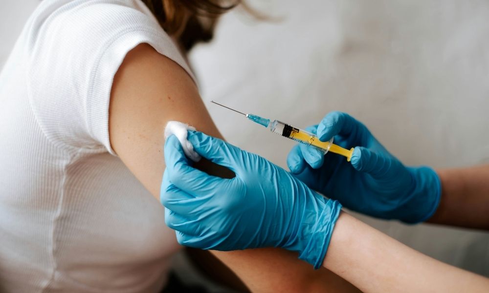 A healthcare worker in blue gloves prepares to give an injection to a patients arm.