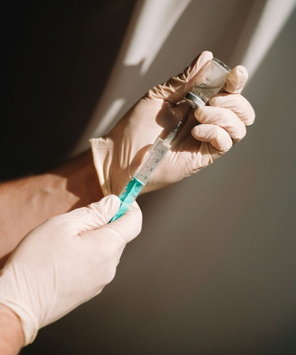 A person wearing latex gloves drawing medication from a glass vial into a syringe.
