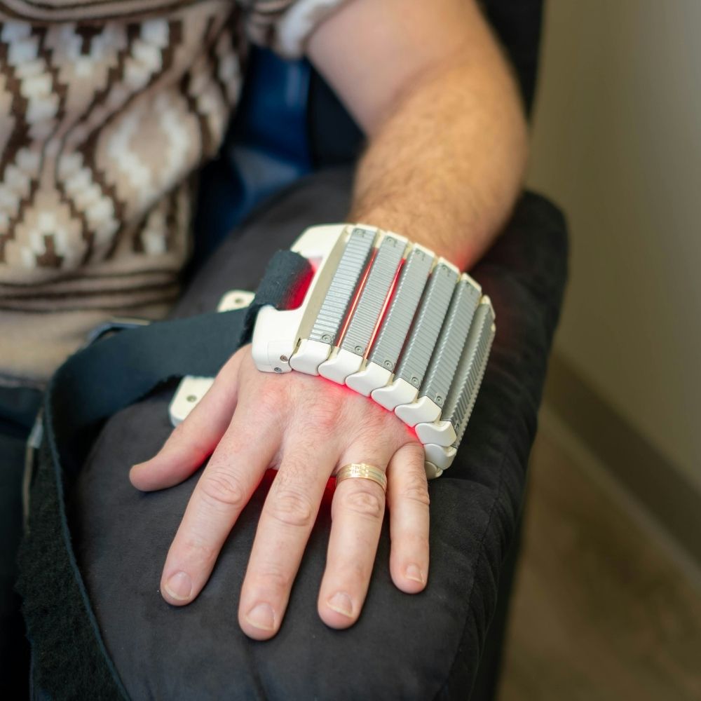 A persons hand resting on an armrest, wearing a segmented red light therapy device across the knuckles.