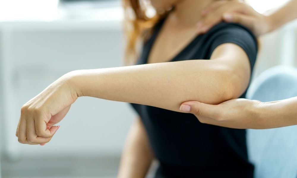 A physical therapist examines a patients elbow.