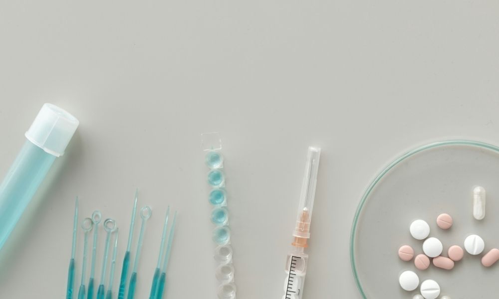 A laboratory test tube, a set of inoculation loops, a strip of capsules, a syringe, and a petri dish containing various tablets.