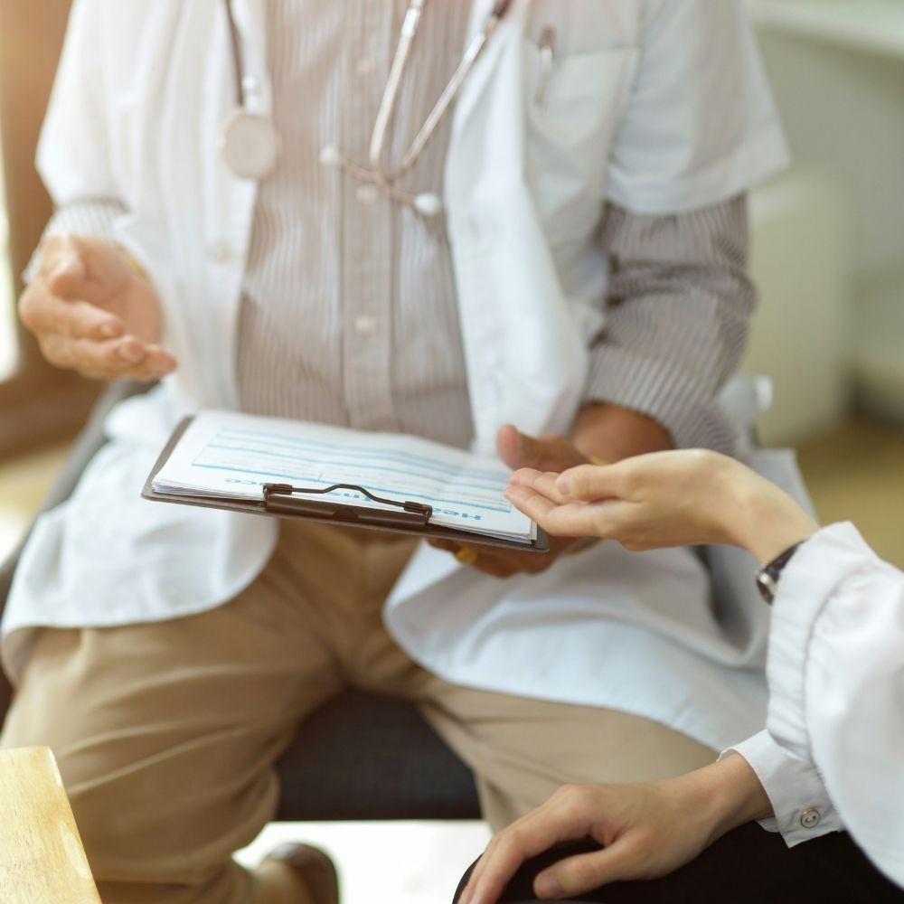 A doctor holding a medical chart speaks with a patient during a consultation.