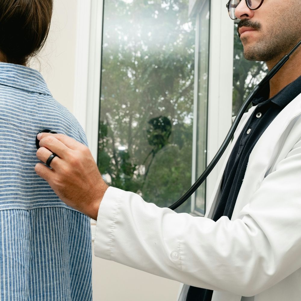 A doctor using a stethoscope to listen to a patients back.
