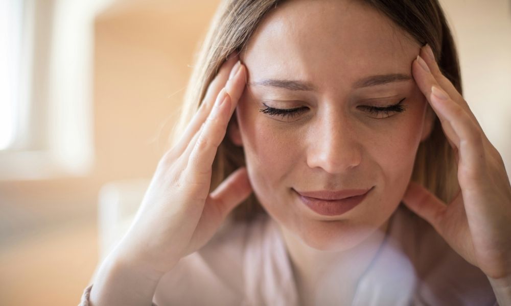 A woman with her eyes closed holds her hands to her temples as if experiencing a headache.