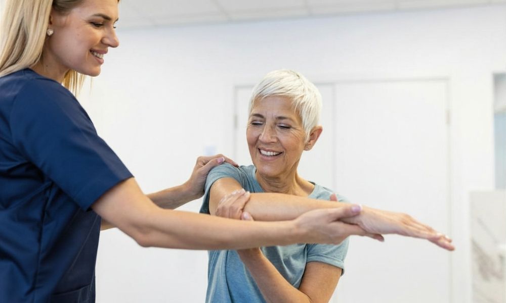A physical therapist assists an older woman with an arm stretching exercise.