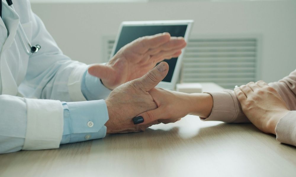 A doctor in a white coat holding a patients hand across a desk.