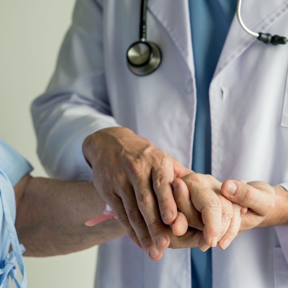 A doctor in a white coat holds the hand of an elderly patient.