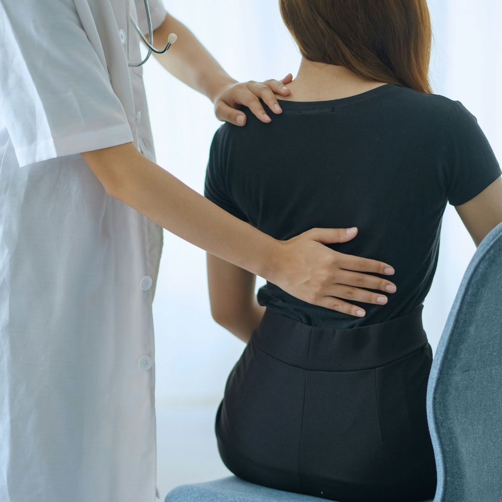 A doctor in a white coat examines a patients back while she sits in a chair.